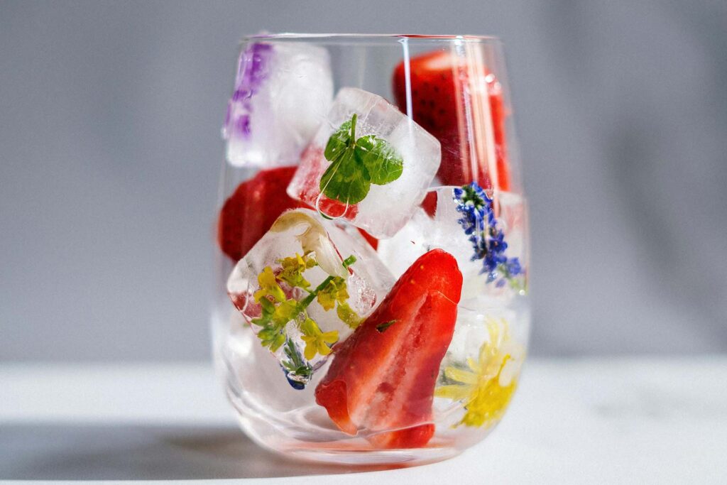 Glass filled with floral and herb-infused ice cubes and strawberries