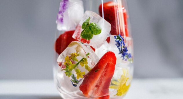 Glass filled with floral and herb-infused ice cubes and strawberries