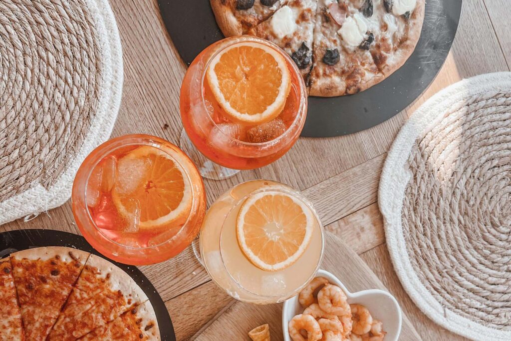 Three orange spritz cocktails on a table with pizza and snacks – spritz cocktail variations