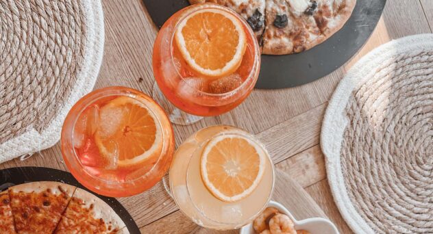 Three orange spritz cocktails on a table with pizza and snacks – spritz cocktail variations